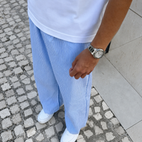 Person wearing a white shirt, light blue pants, and white shoes on a stone pavement.