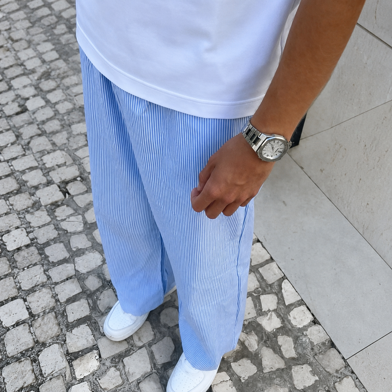 Person wearing a white shirt, light blue pants, and white shoes on a stone pavement.