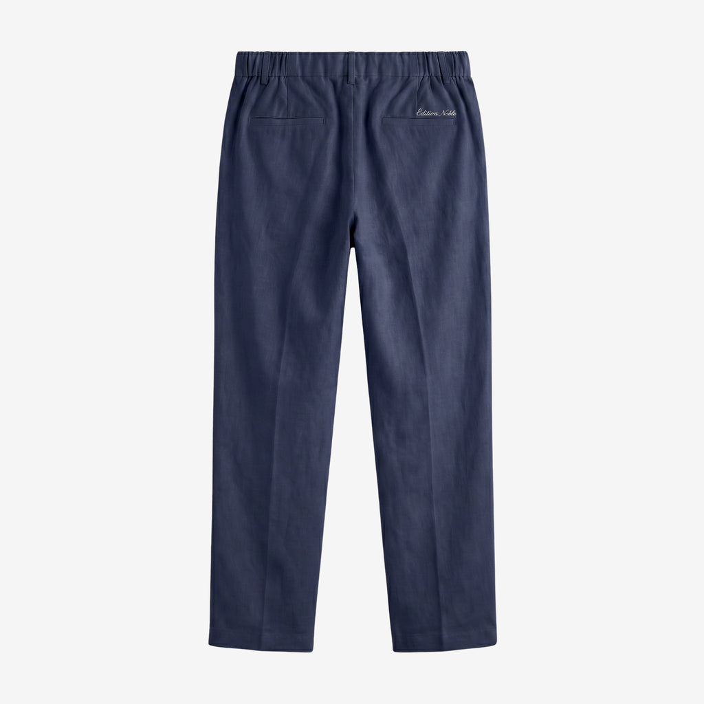 A pair of navy blue trousers shown from the back, featuring an elastic waistband, two back patch pockets, and a small white embroidered logo on the upper right side, set against a plain light gray background.