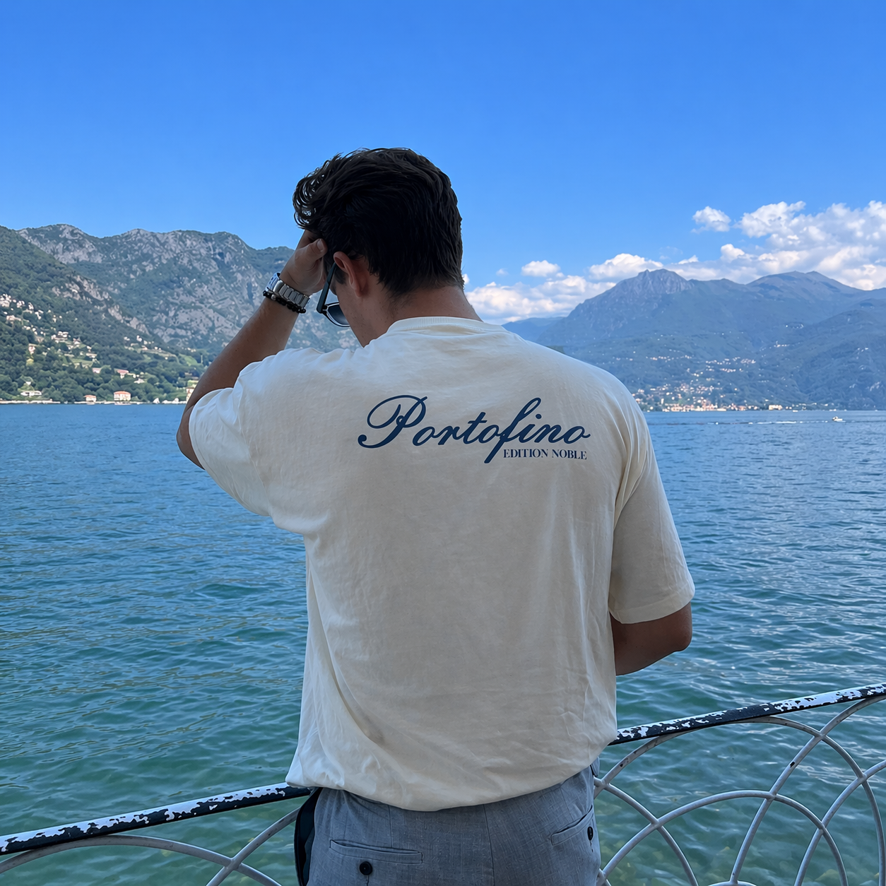 Person wearing a 'Portofino' t-shirt overlooking a scenic view of mountains and water.