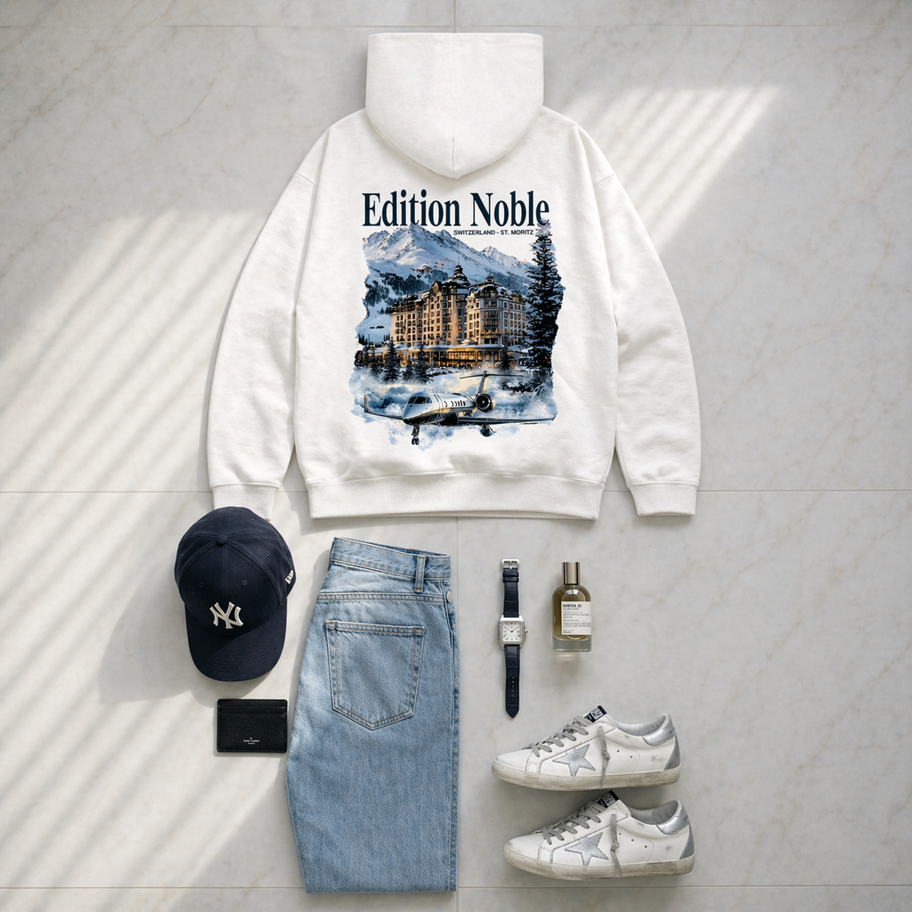White hoodie with 'Edition Noble' design, blue jeans, white sneakers, black cap, wallet, and bottle on a light gray background.