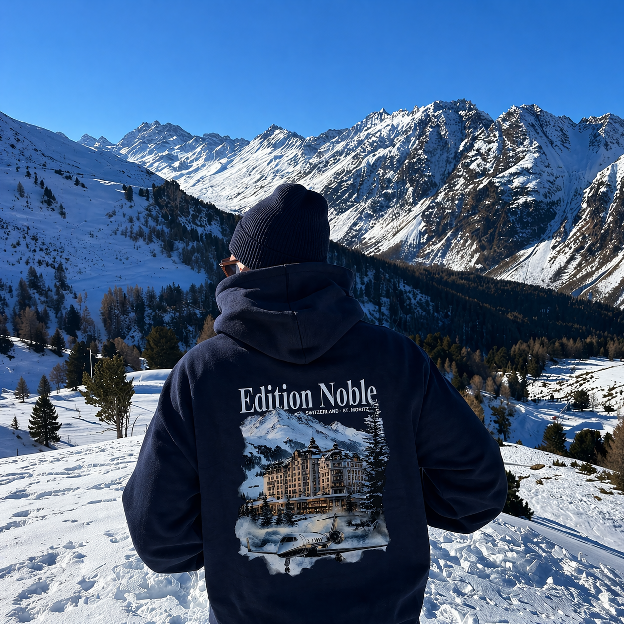 Person wearing a hoodie with 'Edition Noble' design in a snowy mountain landscape