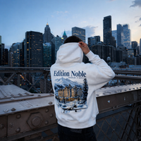 Person wearing a hoodie with 'Edition Noble' branding against a city skyline.