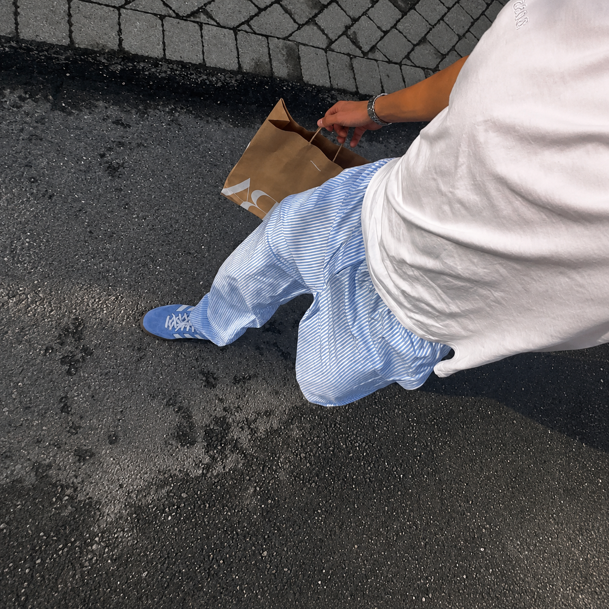 Person wearing a blue shoe and white pants stepping onto a sidewalk.