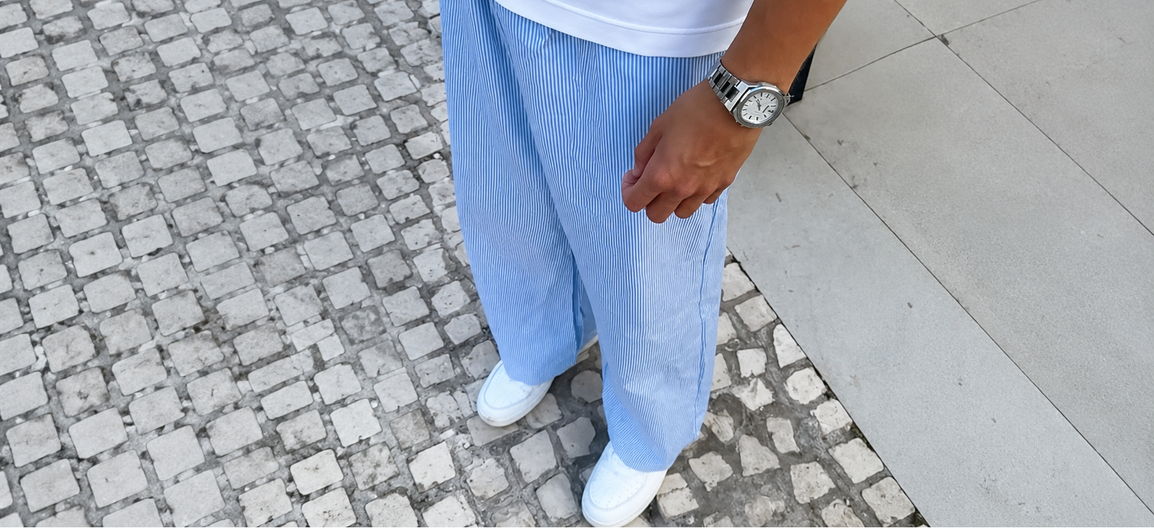 Person wearing light blue pants and a white shirt on a stone pavement.